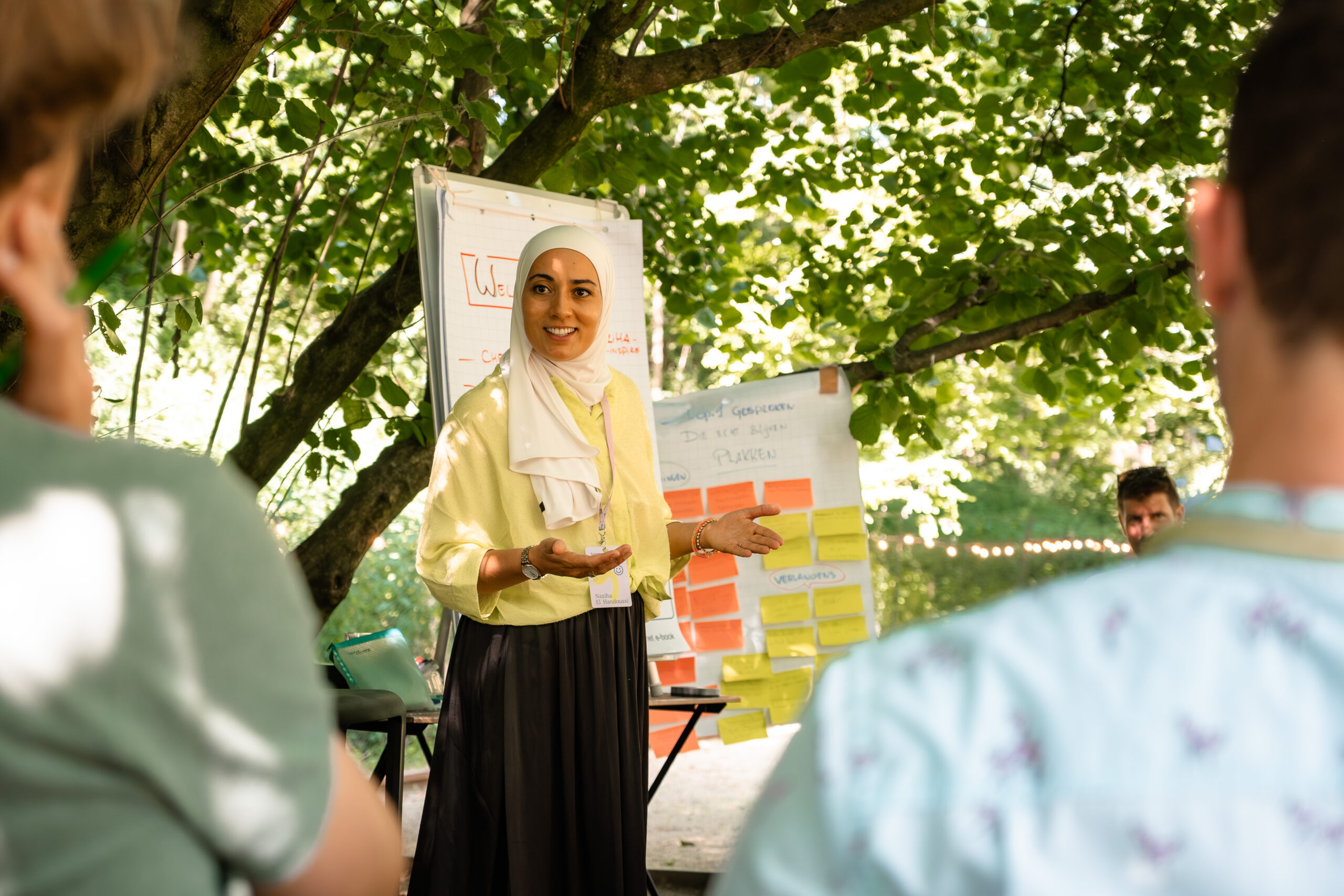 Naziha begeleidt een teambooster sessie buiten met post-its en flipchart — Lead & Inspire